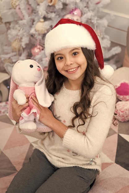 Vacaciones de año nuevo Niño pequeño usar sombrero de santa celebrar el año nuevo en el interior decorado en casa Mañana antes de Navidad Niña en el dormitorio con juguetes Feliz año nuevo Preguntar si la persona tiene una lista de deseos