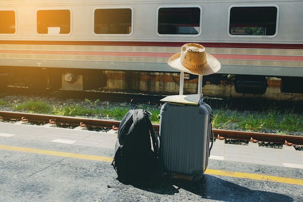 Vacaciones y concepto de viaje. Bolsa de viaje, sombrero de paja y mapa en la estación de tren.