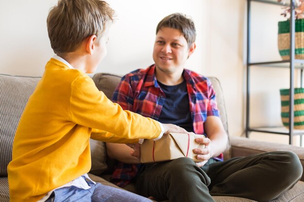 Vacaciones del día del padre Un niño lindo le está dando una caja de regalo hecha a mano a su padre Feliz tiempo en familia juntos, quédense en casa