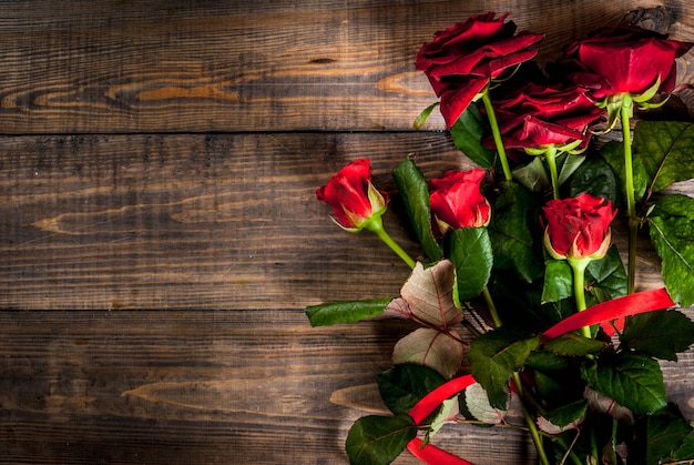 Vacaciones, día de San Valentín. Ramo de rosas rojas, corbata con una cinta roja, con caja de regalo envuelta. En la mesa de madera, vista superior de copyspace