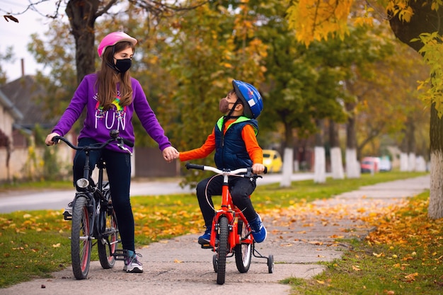 Vacaciones familiares. Hermano y hermana en el parque de otoño divirtiéndose en bicicleta en amapolas hashite. Concepto de pandemia y virus.