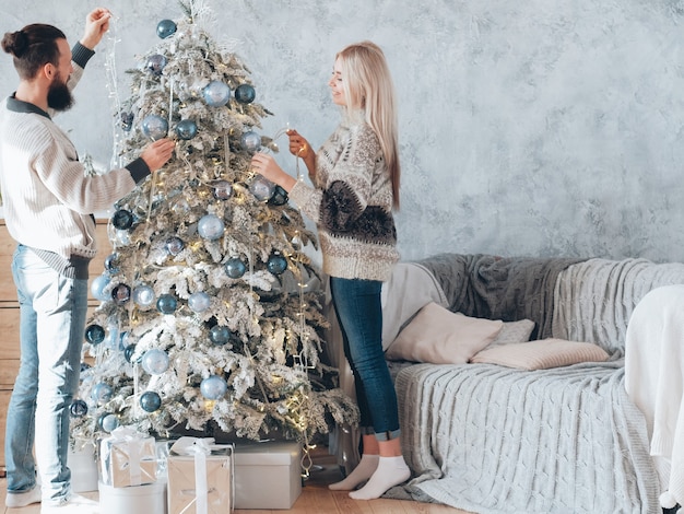 Vacaciones familiares de invierno. Pareja feliz decorar abeto con luces de colores.