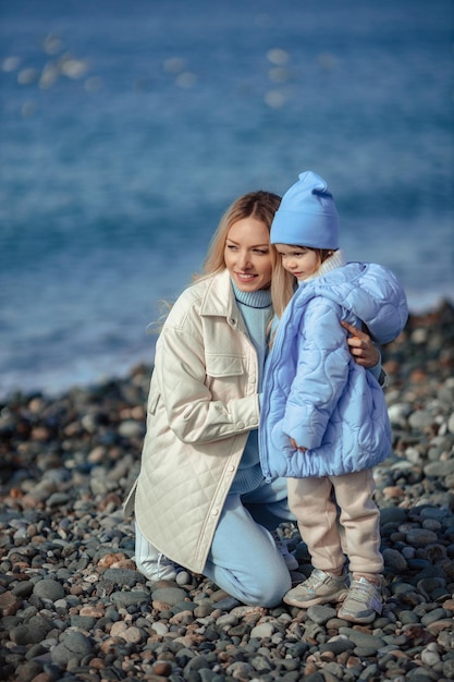 Vacaciones familiares en el mar en otoño o primavera Familia feliz madre e hija en un paseo por la orilla del mar