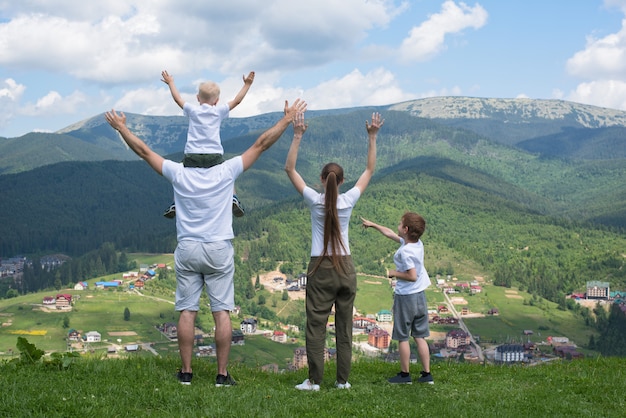 Vacaciones familiares. Padres e hijos se paran con las manos en alto. Montañas en el fondo. Vista trasera.