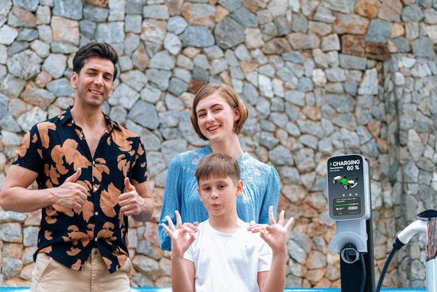 Vacaciones familiares en viaje por carretera con vehículo eléctrico. Precioso vehículo familiar de recarga EV con energía verde y limpia. Fondo de malecón de piedra y viajes en coche ecológicos para un entorno sostenible. Perpetuo.