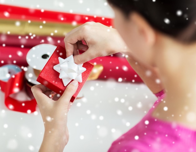 Foto vacaciones, gente y concepto de celebración - cerca de mujer decorando regalo de navidad en casa