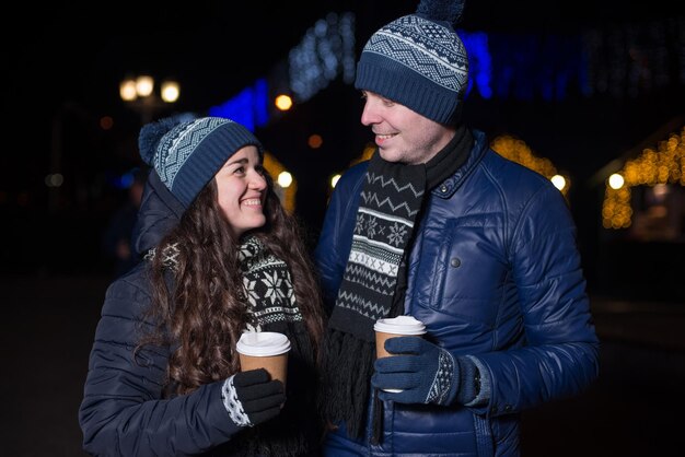 Vacaciones de invierno bebidas calientes y personas concepto feliz pareja joven con café en el mercado de navidad en la noche