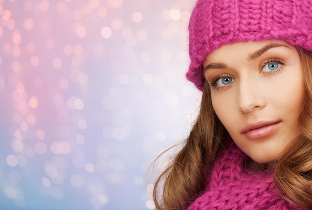 vacaciones de invierno, navidad y concepto de la gente - cerca de una mujer joven con sombrero y bufanda sobre fondo de luces de cuarzo rosa y serenidad