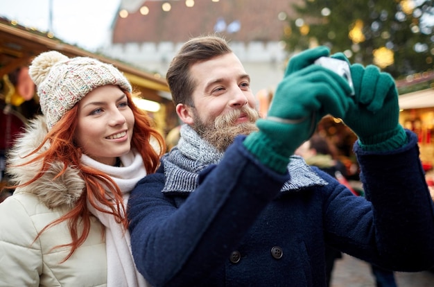 vacaciones, invierno, navidad, tecnología y concepto de personas - feliz pareja de turistas en ropa de abrigo tomando fotos con cámara en el casco antiguo