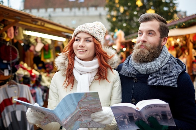 vacaciones, invierno, navidad, turismo y concepto de personas - pareja feliz en ropa de abrigo con mapa y guía de la ciudad en el casco antiguo