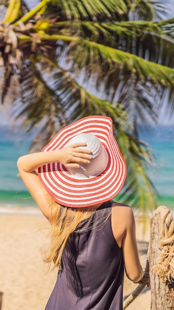 Vacaciones en una isla tropical mujer con sombrero disfrutando de la vista al mar desde un puente de madera en formato vertical para