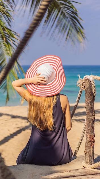 Vacaciones en una isla tropical mujer con sombrero disfrutando de la vista al mar desde un puente de madera en formato vertical para