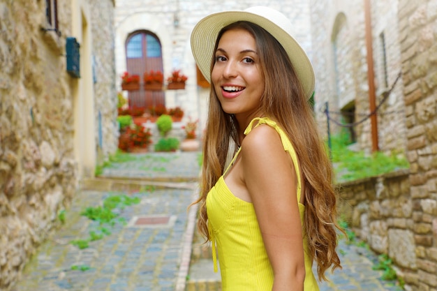 Vacaciones en Italia. Retrato de mujer joven con sombrero y vestido amarillo caminando en el pueblo italiano de Asís, Umbría.