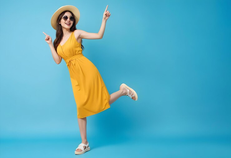vacaciones joven mujer asiática con un vestido amarillo gafas de sol y un sombrero de paja posando y apuntando