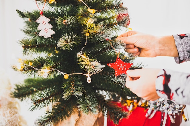 Vacaciones de Navidad y año nuevo. Primer plano de las manos del niño decorando arbolito de Navidad durante. Niño en pijama colgando juguetes de madera decorativos en ramas de abeto. Estilo de vida de vacaciones de invierno.