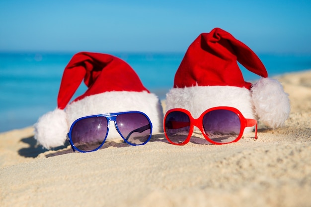 Vacaciones de Navidad y Año Nuevo Romántico en el Mar. Gorro de Papá Noel y gafas de sol en la playa de arena