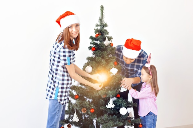 Vacaciones, Navidad y concepto de celebración - Familia feliz decorando el árbol de Navidad en vacaciones sobre fondo blanco.