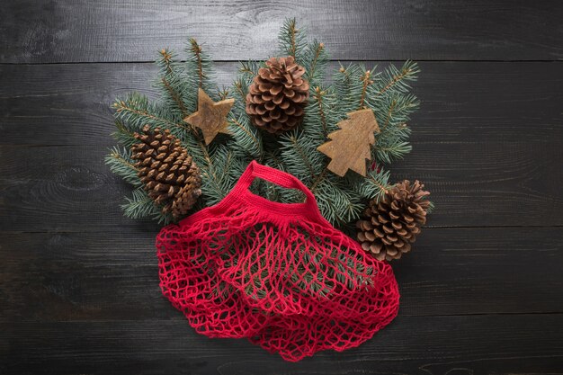 Vacaciones de Navidad sin desperdicio. Ramas de abeto conífero en bolsa ecológica de algodón rojo sobre tabla negra. Eco amigable Navidad.