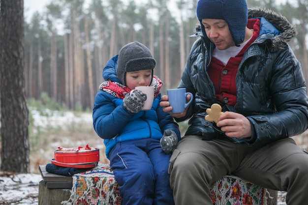 Vacaciones de Navidad, padre e hijo bebiendo bebidas calientes de año nuevo. Familia feliz en un paseo al aire libre en el soleado bosque de invierno