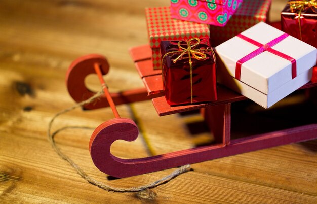 vacaciones, navidad, regalos, año nuevo y concepto de celebración - cierre de muchas pequeñas cajas de regalo en trineo de madera roja sobre mesa de madera