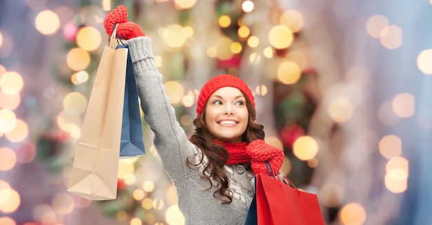 Foto vacaciones, navidad, venta y concepto de la gente - joven asiática feliz vestida de invierno con bolsas de compras sobre el fondo de las luces del árbol de navidad
