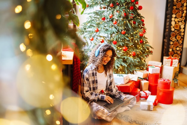 Vacaciones navideñas en línea La mujer joven usa una computadora portátil para hacer una videollamada con su familia o amigos