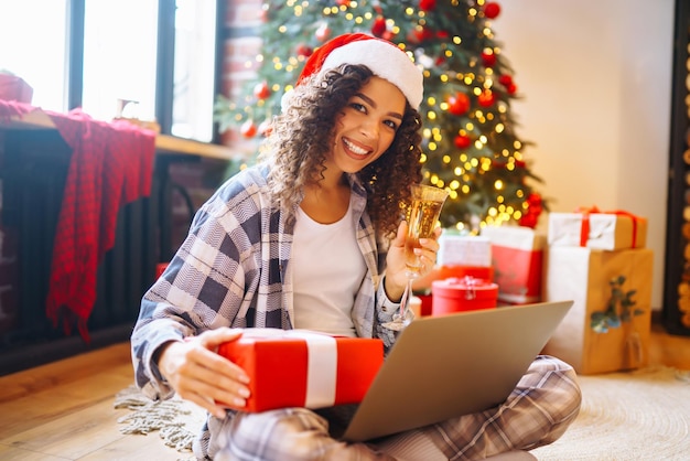 Vacaciones navideñas en línea La mujer joven usa una computadora portátil para hacer una videollamada con su familia o amigos