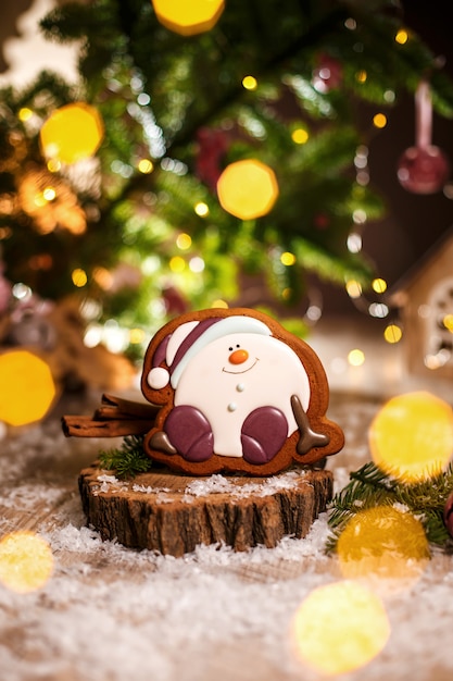Vacaciones panadería comida tradicional. Pan de jengibre feliz sentado Muñeco de nieve o bola de nieve en una acogedora decoración cálida con luces de guirnalda