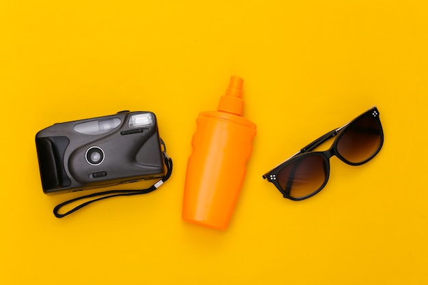 Vacaciones en la playa, concepto de viaje. Botella de bloqueador solar, gafas de sol y cámara en amarillo.