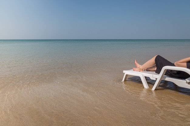 Vacaciones en playa tropical Piernas de mujer en la cama de la playa con fondo de agua clara del océano