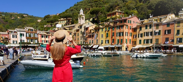 Vacaciones en Portofino Italia Vista posterior de una hermosa chica vestida de rojo disfrutando de la vista del pintoresco pueblo de Portofino con barcos amarrados y gente caminando en la pancarta panorámica de la plaza Piazzetta