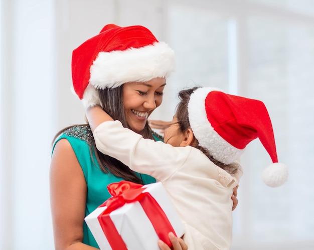 vacaciones, regalos, navidad, concepto de navidad - feliz madre e hija niña con sombreros de ayudante de santa con caja de regalo