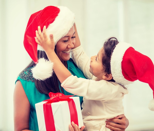 vacaciones, regalos, navidad, concepto de navidad - feliz madre e hija niña con sombreros de ayudante de santa con caja de regalo