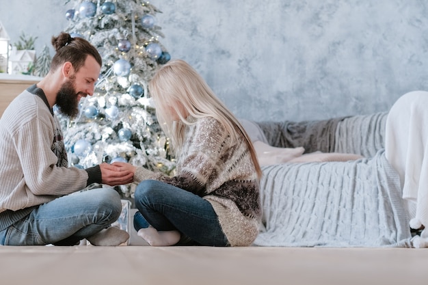 Vacaciones románticas de invierno. Vista lateral de la pareja sentada con las piernas cruzadas en el suelo, tomados de la mano