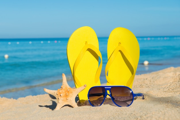 Vacaciones soleadas en la playa positivas. Sandalias amarillas, gafas de sol y estrellas de mar sobre un fondo del mar