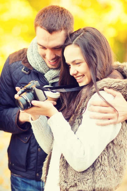 vacaciones, tecnología, gente feliz, concepto de citas - pareja con cámara de fotos en el parque de otoño