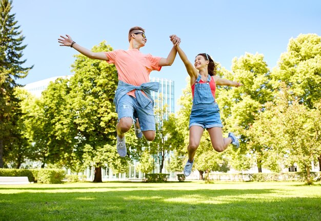 Foto vacaciones, vacaciones, amor y concepto de la gente - feliz pareja adolescente sonriente saltando en el parque de verano