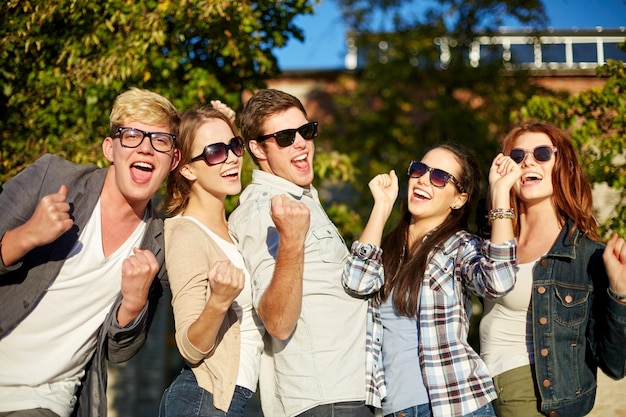 vacaciones de verano, amistad, logro y concepto de éxito - grupo de amigos felices que muestran un gesto de triunfo en el campus o en el parque de la ciudad