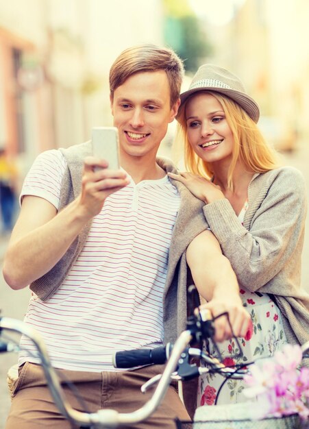 vacaciones de verano, aplicaciones y concepto de citas - pareja con bicicletas y smartphone en la ciudad