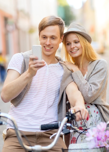 vacaciones de verano, bicicletas, amor, relación, navegación, gps y concepto de citas - pareja con bicicletas y teléfonos inteligentes en la ciudad