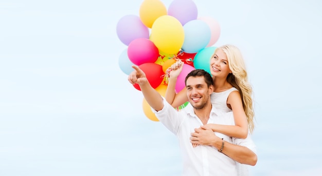 vacaciones de verano, celebración y concepto de citas - pareja con globos de colores al lado del mar