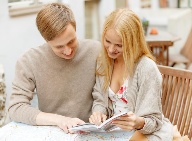 Vacaciones de verano, citas, escapadas urbanas y concepto de turismo: pareja feliz con mapa, cámara y guía de viajeros en la cafetería.