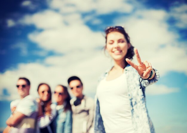 vacaciones de verano y concepto adolescente - cierre de la mano femenina que muestra el signo v con los dedos con amigos en la espalda