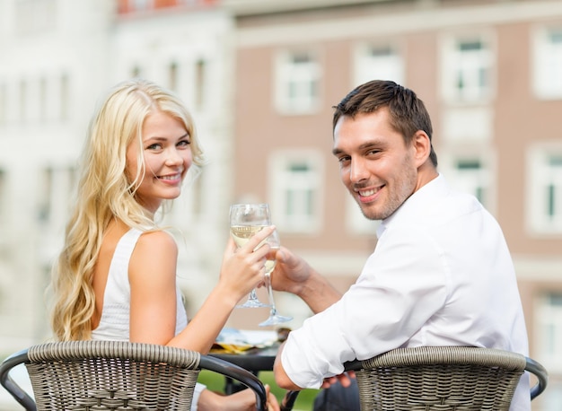 Vacaciones de verano y concepto de citas - pareja sonriente bebiendo vino en la cafetería de la ciudad