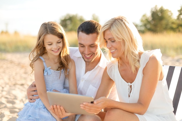 vacaciones de verano, concepto de familia, niño y tecnología - familia sonriente en la playa con computadora de tablet pc