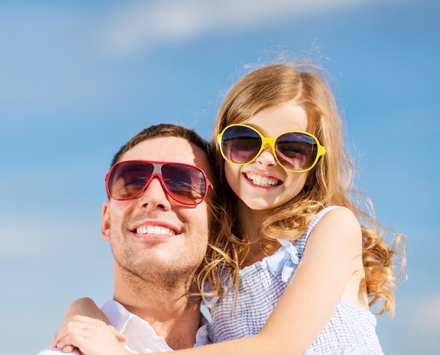 Vacaciones de verano, concepto de niños y personas - feliz padre e hijo en gafas de sol sobre el cielo azul