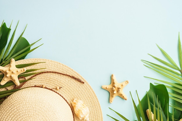 Vacaciones de verano y concepto de viaje Hojas de palma sombrero y conchas de mar sobre fondo azul Plano con espacio de copia