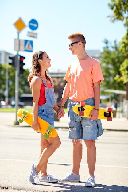 vacaciones de verano, deporte extremo y concepto de la gente - pareja adolescente feliz con monopatines de crucero modernos y cortos hablando en la calle de la ciudad