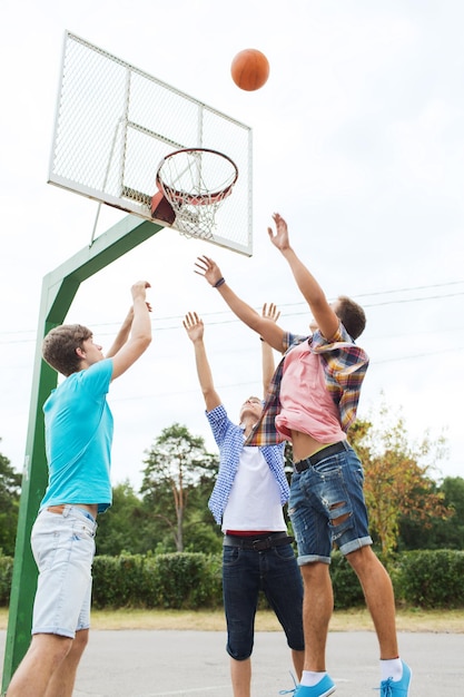 vacaciones de verano, deporte, juegos y concepto de amistad - grupo de amigos adolescentes felices jugando baloncesto al aire libre