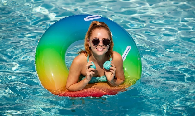 Foto vacaciones de verano. disfrutando del bronceado. mujer en traje de baño en círculo inflable en la música de los auriculares de la piscina.